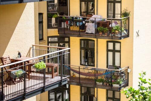 Stålaltaner med flotte møbler, planter og hængekøje på gul facade i flot baggård i København