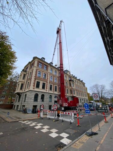 Stor mobilkran der løfter materialer til altanprojekt over et hustag.