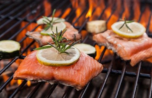 Laks med citron og rosmarin ved at stege på skindsiden på en gril med åbne flammer.